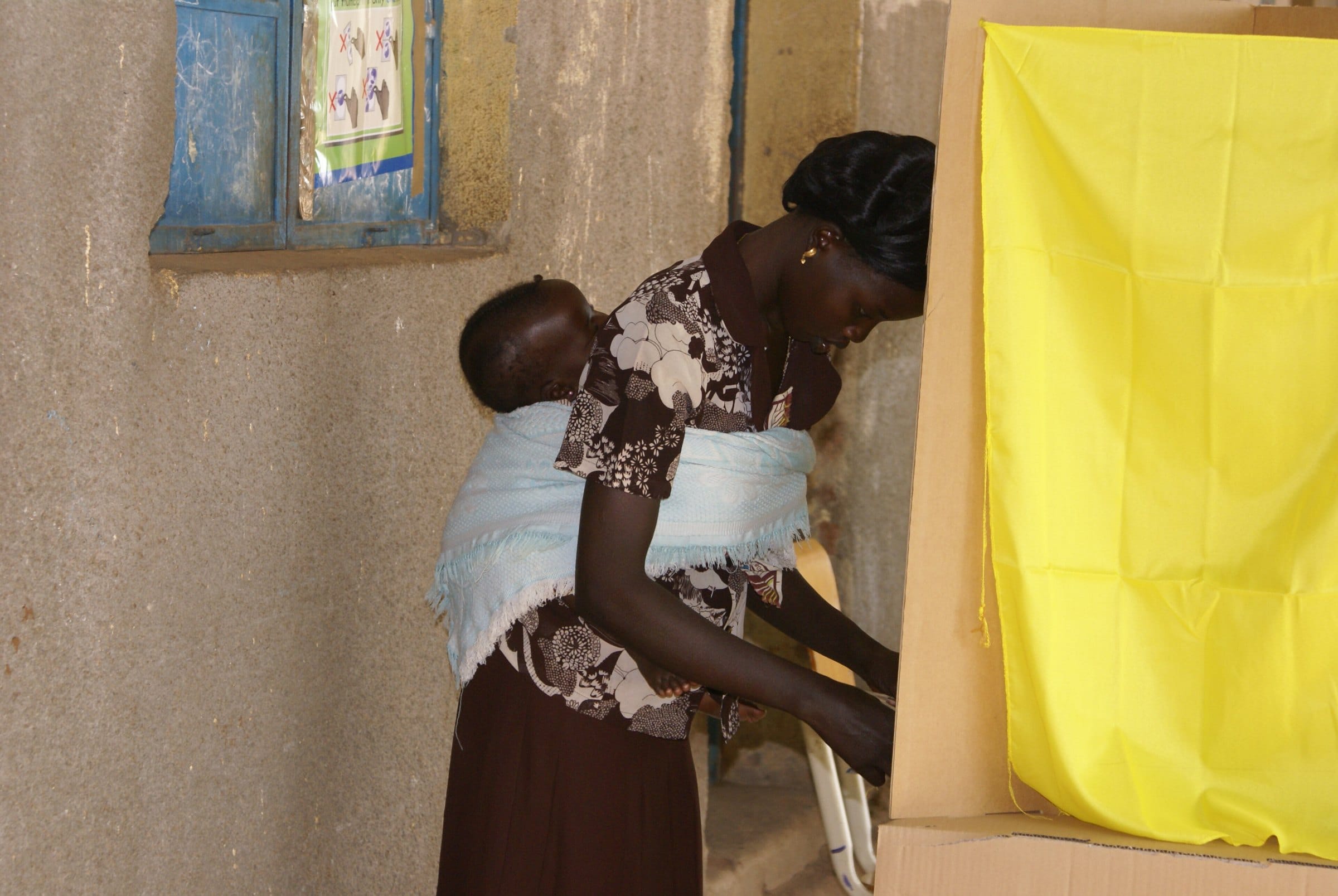 A mother carrying her baby casts her vote in a booth